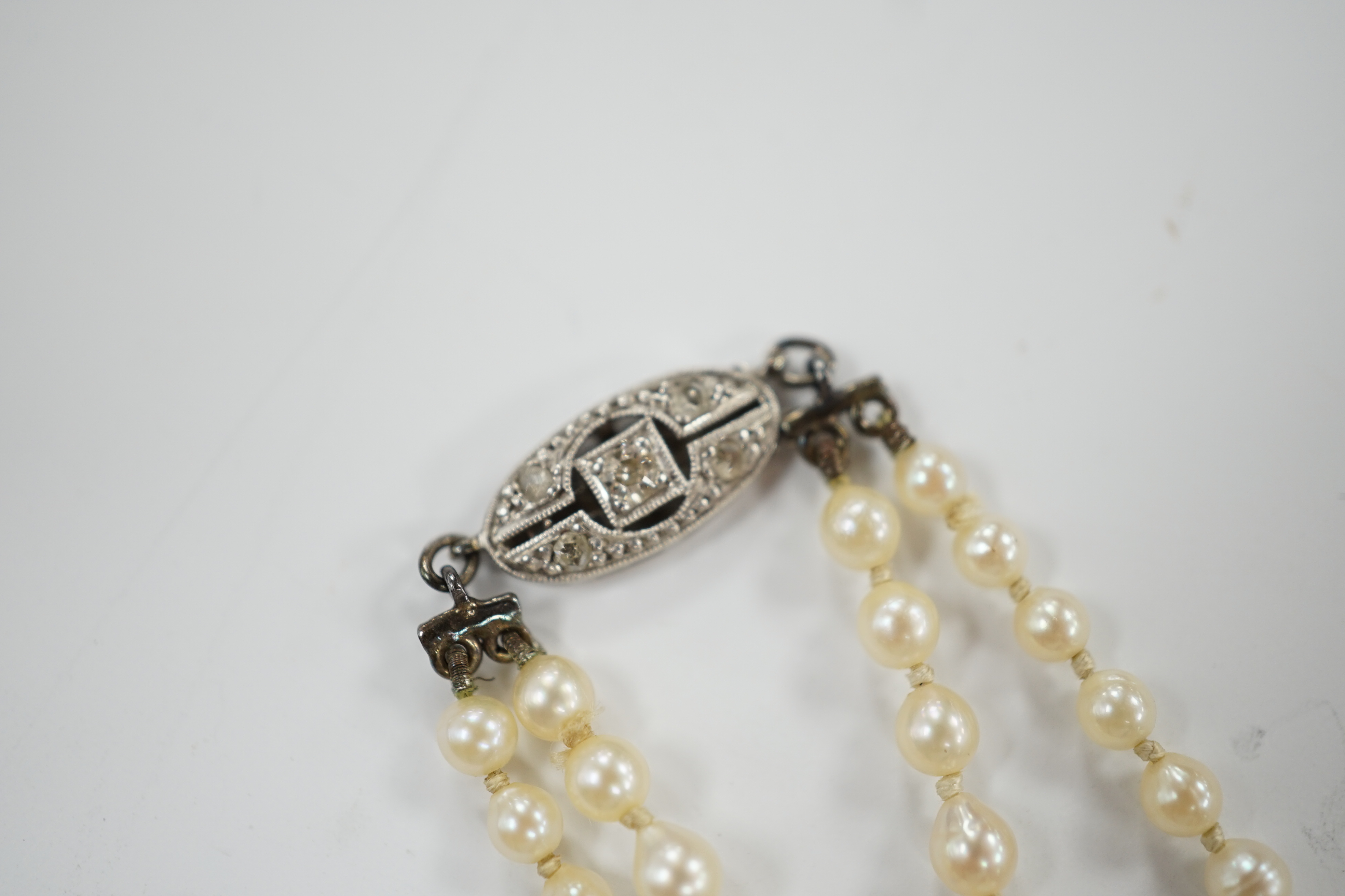 A 1930's twin strand graduated cultured pearl necklace, with 14ct, plat and diamond chip set clasp, 50cm.